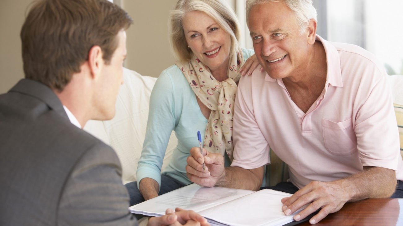 Senior Couple Meeting With Financial Advisor At Home And Smiling