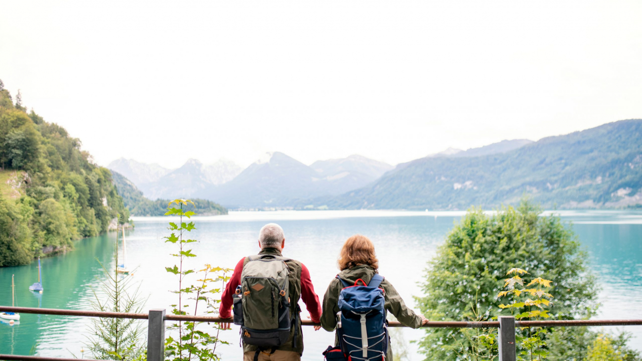 A rear view of senior pensioner couple standing by lake in nature. Copy space.