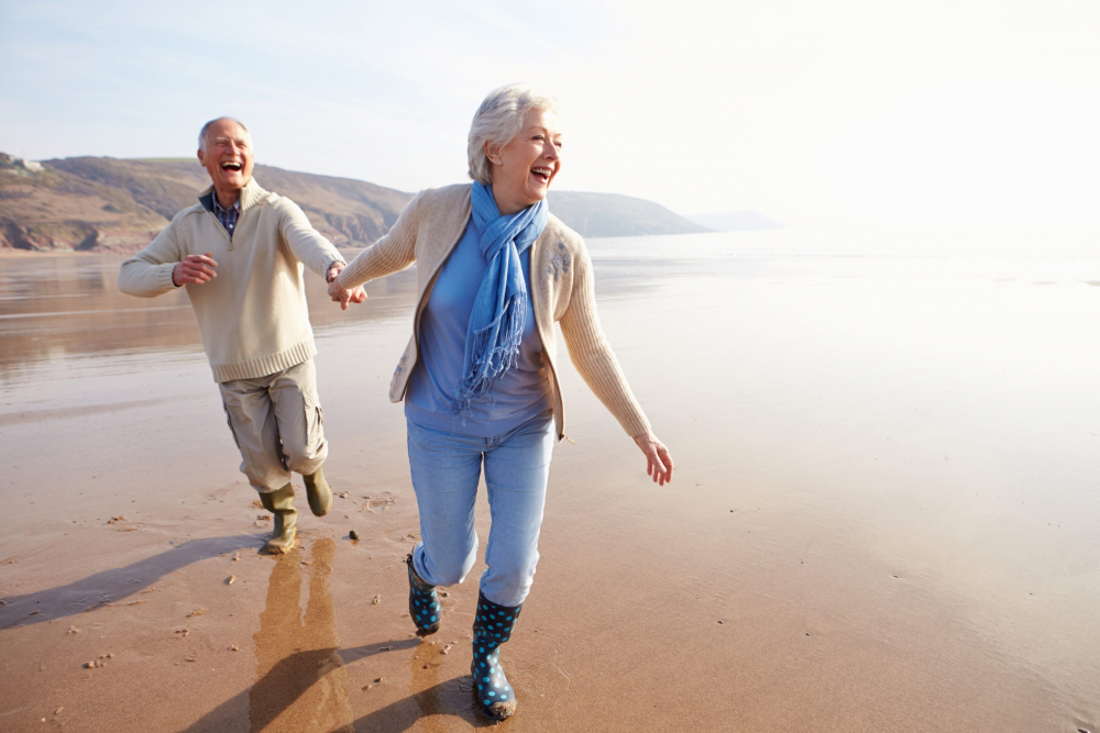 Senior Couple Running Along Winter Beach Laughing